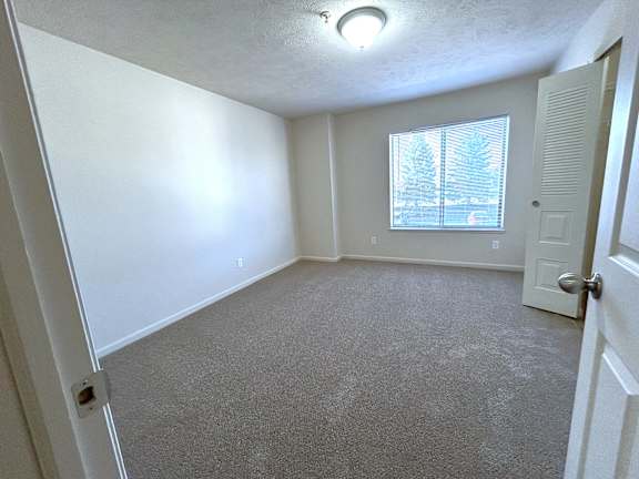 Empty carpeted room with window and ventilated closet door at Heatherwood Apartments, Grand Blanc, MI 48439