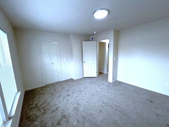 Vacant carpeted bedroom with closet and open hallway door at Heatherwood Apartments, Grand Blanc, 48439