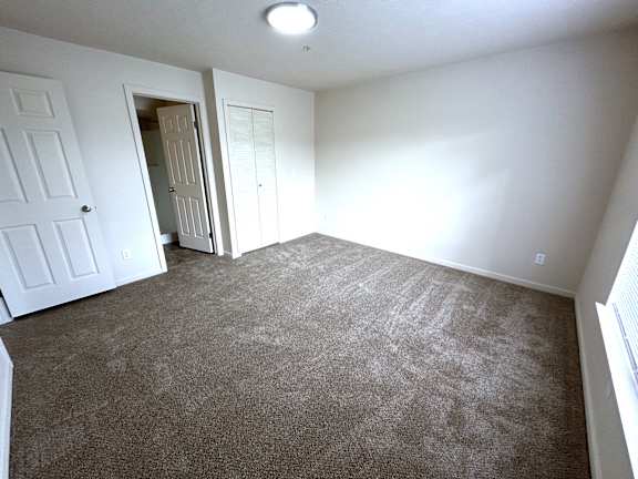 Empty carpeted bedroom with closet and two doorways at Heatherwood Apartments, Grand Blanc, MI 48439