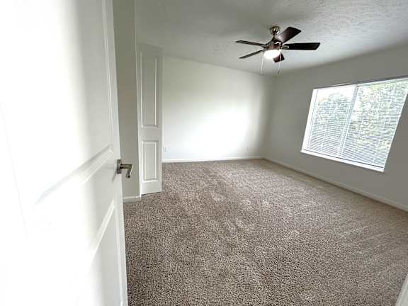 Spacious carpeted bedroom with ceiling fan and window at Heatherwood Apartments, Michigan
