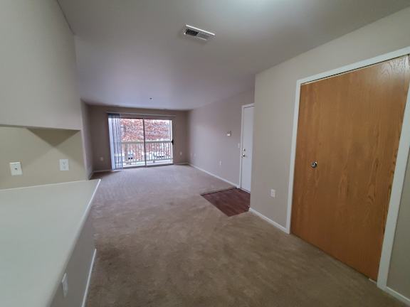 A living room and dining room with a brown door and a window with a view.