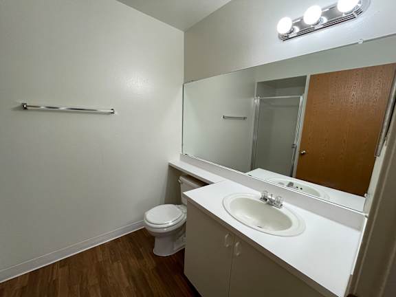 A white bathroom with a toilet, sink, mirror and lights.