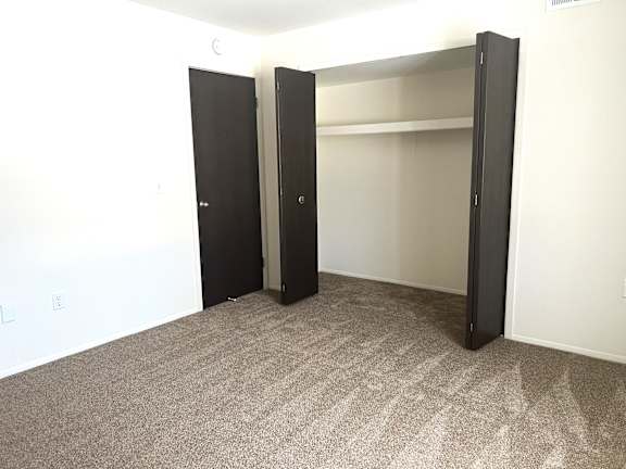 A bedroom with a carpeted floor and two open closets.