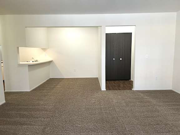 A living room and dining room with a black door and a grey carpet.