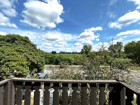 A view from a balcony overlooking a road with trees and a blue sky with clouds.