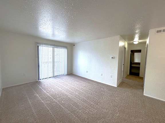A living room with a carpeted floor and a window with blinds.