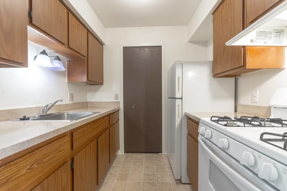 a kitchen with wooden cabinets and white appliances at The Landings Apartments, Westland