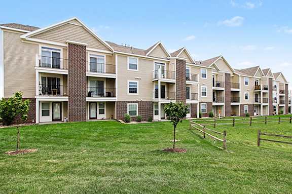 Apartment building with balconies and patios and a green lawn with trees at Andover Pointe Apartment Homes in La Vista, NE