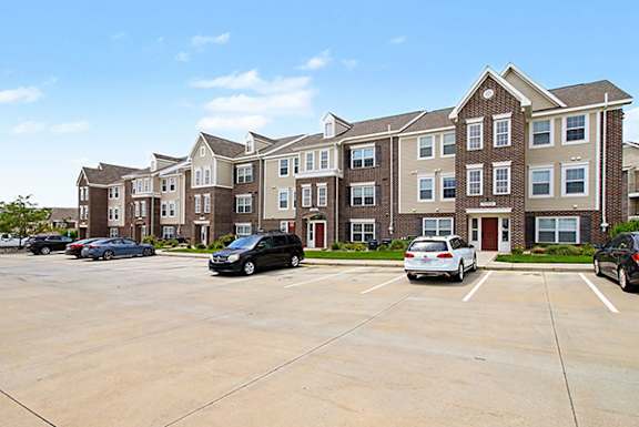A parking lot in front of a large apartment building with cars parked at Andover Pointe Apartment Homes in La Vista, NE
