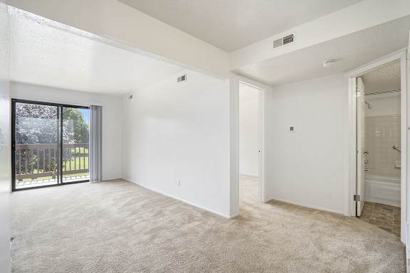 A spacious living room with a carpeted floor and sliding glass doors leading to a balcony at Apple Ridge Apartments, Michigan, 49534