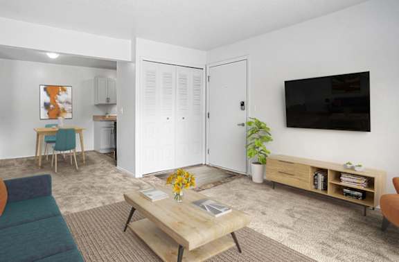 A living and dining room with a blue couch, a wooden coffee table, and a flat screen TV mounted on the wall at Apple Ridge Apartments in Walker, MI