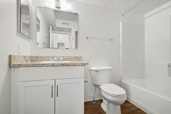 A white bathroom with a marble counter top and a toilet.