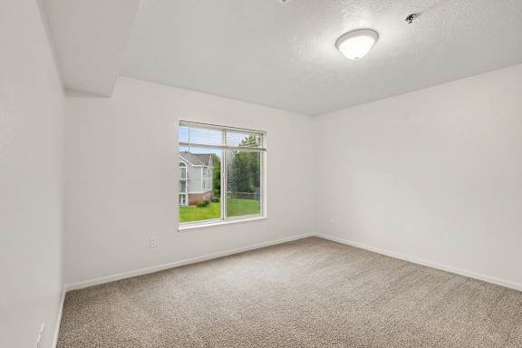 A room with a carpeted floor and a window showing a view of a house.