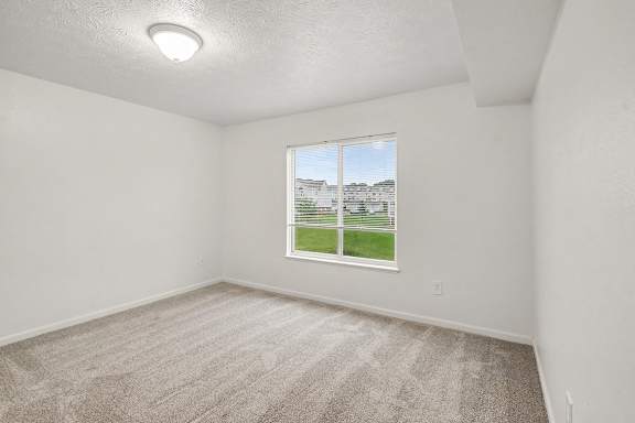 A room with a carpeted floor and a window showing a view of a house.
