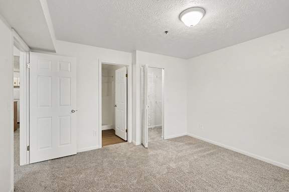 A room with white walls and carpeted floor with three doors.
