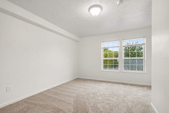 A bedroom with a carpeted floor and a window showing a tree at Autumn Lakes Apartments and Townhomes in Mishawaka, IN