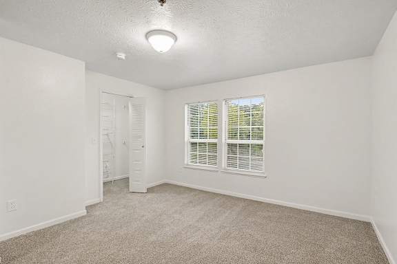 A room with a carpeted floor, a walk-in closet, and a window with blinds at Autumn Lakes Apartments and Townhomes in Mishawaka, IN