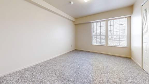 A room with a carpeted floor and a window with blinds.