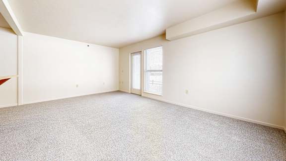A spacious room with a carpeted floor and a door leading to a window.