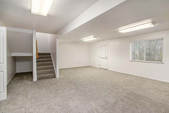 A spacious recreation room with a staircase and a window with blinds at Autumn Lakes Apartments and Townhomes, Mishawaka, 46544