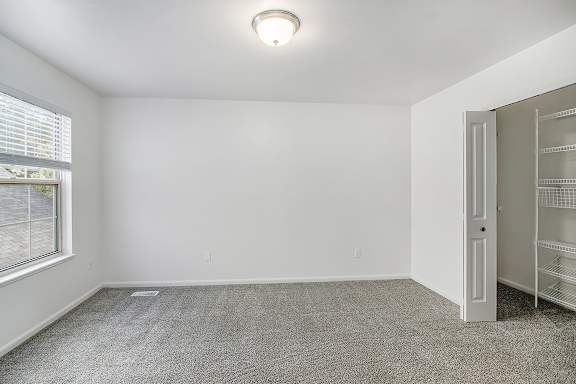 A bedroom with a carpeted floor, a window with blinds, and a walk-in closet with organizers at Autumn Lakes Apartments and Townhomes, Mishawaka, 46544