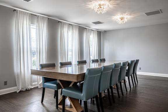 A long wooden table with blue chairs is in the middle of a room with a window at Pheasant Run Apartments, Indiana, 47909