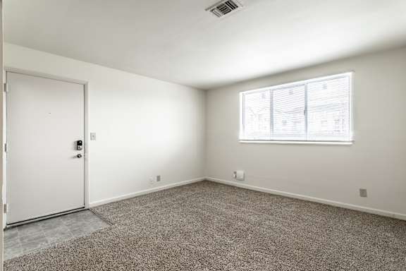 A room with a carpeted floor, a white door, and a window with blinds at Bay Pointe Apartments, Indiana, 47909