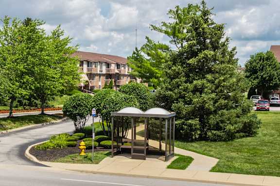 A bus stop with a bench and a yellow fire hydrant in front of a building at Bay Pointe Apartments, Lafayette, IN