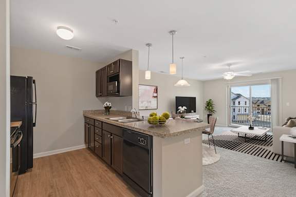 A kitchen with a refrigerator, sink, and a counter with a bowl of fruit on it.