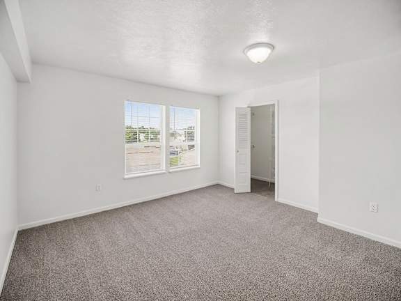 A bedroom with a carpeted floor, a walk-in closet, and a view of the outdoors through the windows at Black Sand Apartments Homes, Lincoln, NE 68504