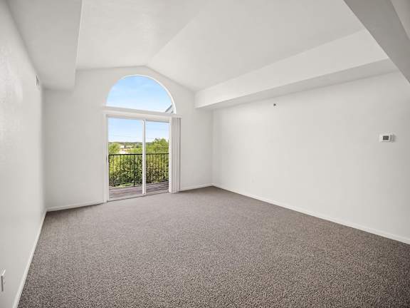 A living room with a cathedral ceiling, carpeted floor and a large window with a view of the outdoors at Black Sand Apartments Homes, Lincoln, NE 68504