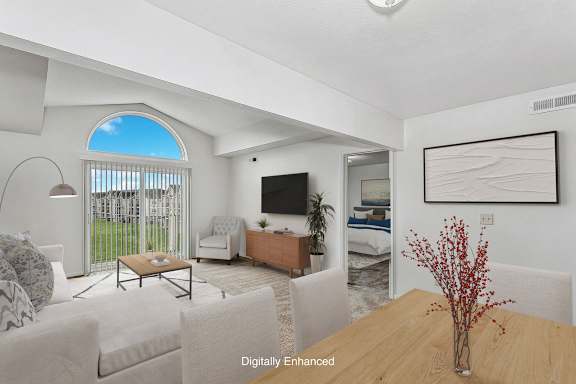 A living room with a cathedral ceiling, television, a couch, a chair, a table, and a vase with red flowers at Black Sand Apartment Homes, Lincoln, Nebraska