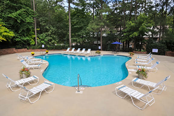 A pool surrounded by chairs and trees.
