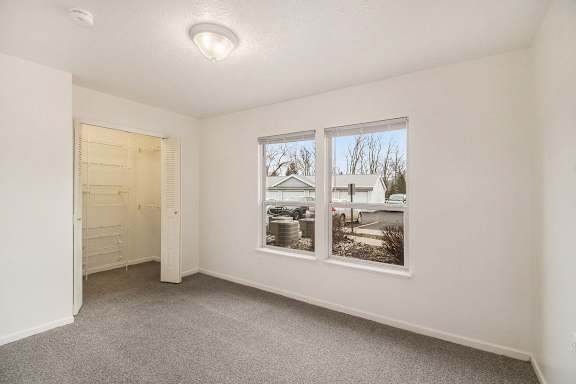 A bedroom with a carpeted floor, a walk in closet, and large windows at Brentwood Park Apartments in LaVista, NE