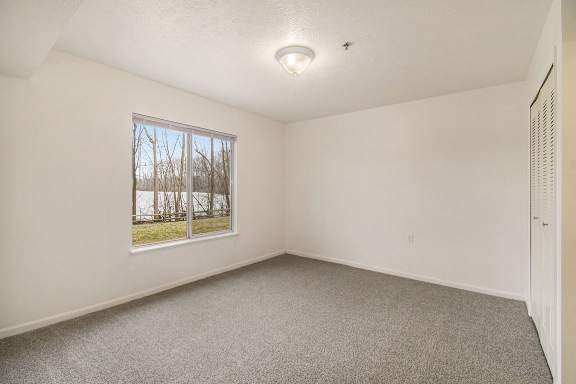 A bedroom with a window and a carpeted floor at Brentwood Park Apartments in LaVista, NE