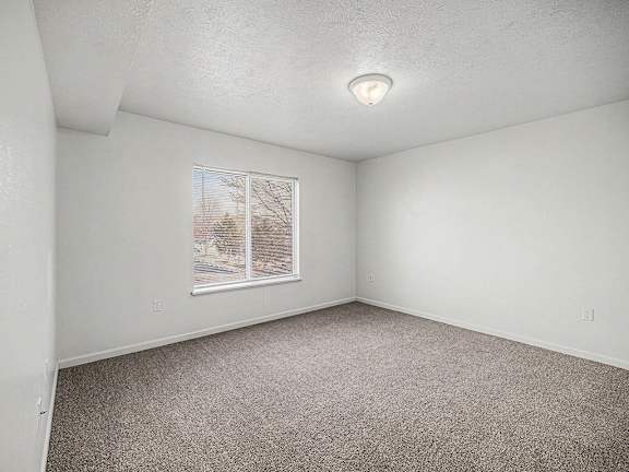 A bedroom with a large window and carpeted floor at Brentwood Park Apartments in LaVista, NE