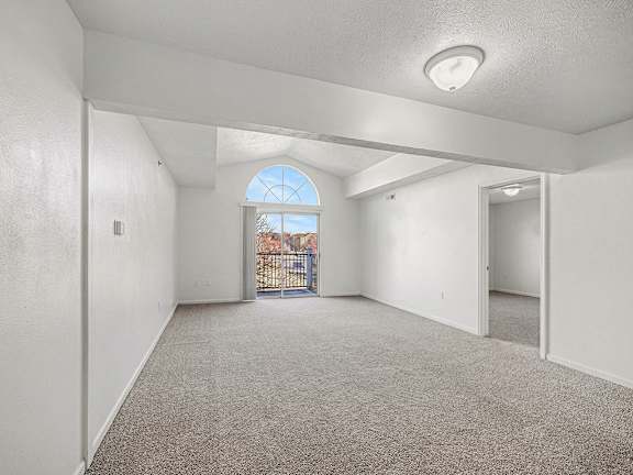 A spacious living room with a carpeted floor and a cathedral ceiling at Brentwood Park Apartments in LaVista, NE