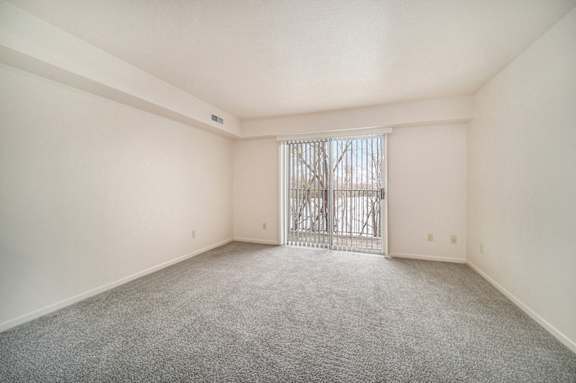 A living room with a carpeted floor and a slider to a balcony at Brentwood Park Apartments in LaVista, NE