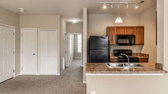 A kitchen with a black fridge and microwave, and a hallway with white doors