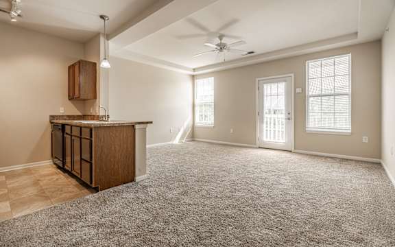 A spacious living room with a carpeted floor and a ceiling fan