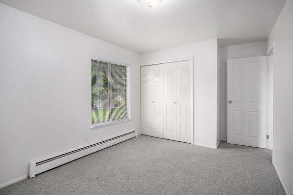 A bedroom with white walls and a window with blinds at Brookside Apartments, Springfield