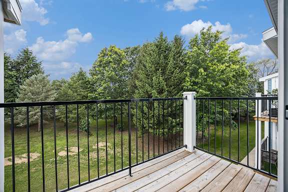 A balcony with a black railing overlooks a grassy area with trees at Byron Lakes Apartments in Byron Center, MI