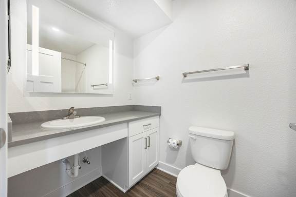 A white toilet sits next to a sink and mirror in a bathroom at Byron Lakes Apartments in Byron Center, MI