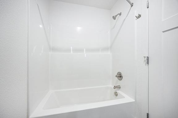 A white bathroom with a tub and shower at Byron Lakes Apartments in Byron Center, MI