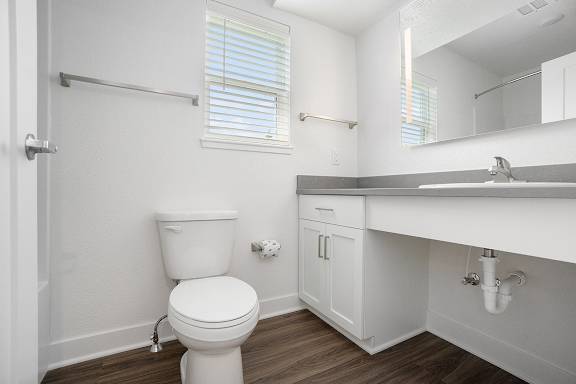 A bathroom with a window, toilet with a white cabinet and sink at Byron Lakes Apartments, Byron Center, Michigan