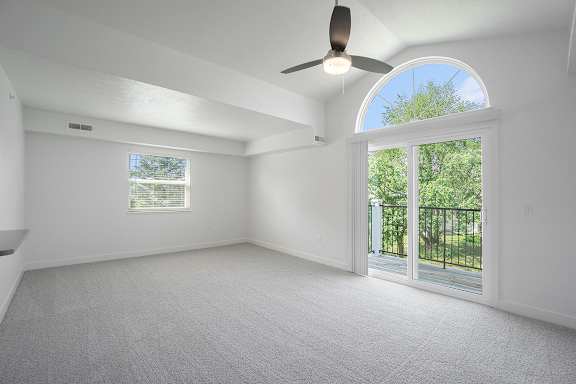 An enlarged living room with a cathedral ceiling, ceiling fan and sliding glass doors leading to a balcony at Byron Lakes Apartments, Michigan, 49315