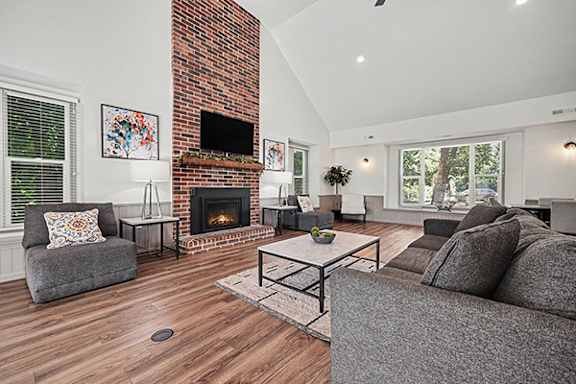 A community room with a fireplace and a grey couch at Byron Lakes Apartments in Byron Center, MI