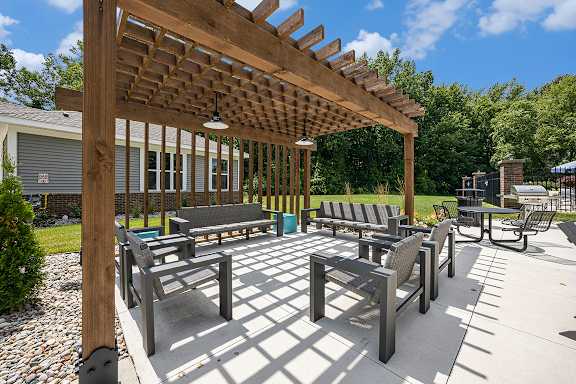 A wooden pergola with benches in a sunny outdoor area at Byron Lakes Apartments, Byron Center, MI