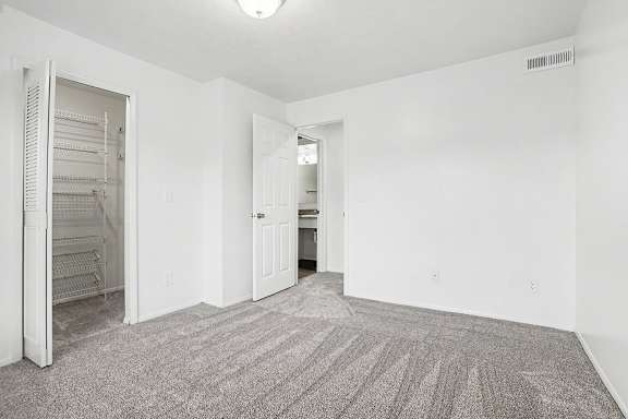 A spacious bedroom with a carpeted floor and a walk-in closet with organizers at Canal Club Apartments in Lansing, MI
