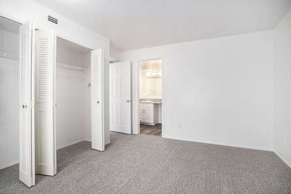 A white bedroom with a carpeted floor and an ensuite bathroom at Canal Club Apartments in Lansing, MI